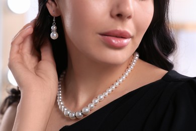 Young woman wearing elegant pearl jewelry indoors, closeup