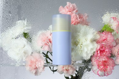 Bottle with moisturizing cream and beautiful flowers on light background, view through wet glass