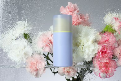 Photo of Bottle with moisturizing cream and beautiful flowers on light background, view through wet glass