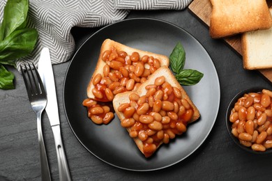 Toasts with delicious canned beans on black table, flat lay