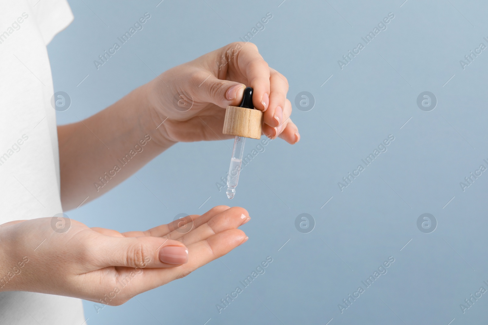 Photo of Woman dripping serum from pipette on her hand against light grey background, closeup. Space for text