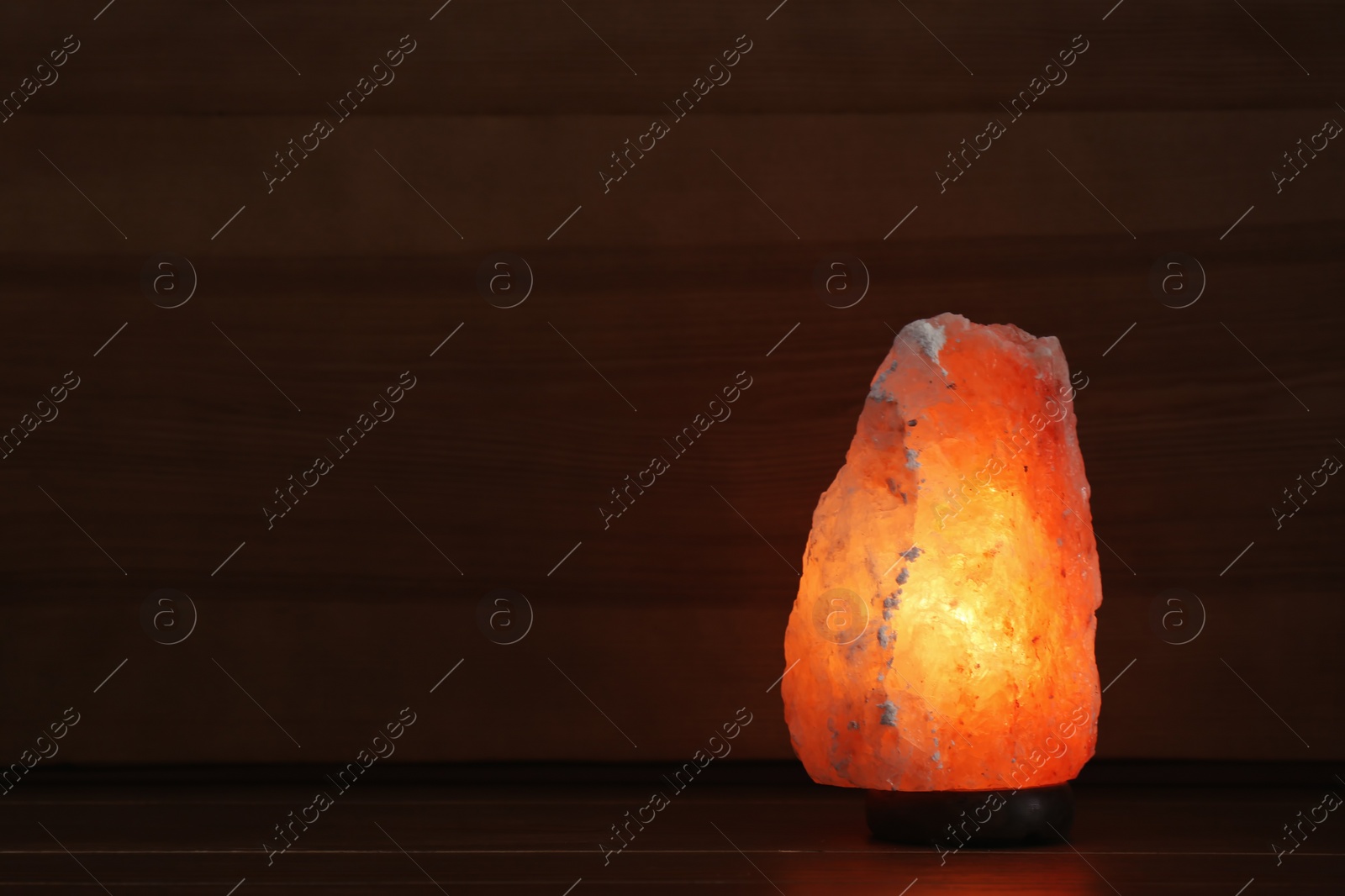 Photo of Himalayan salt lamp glowing on dark background with space for text