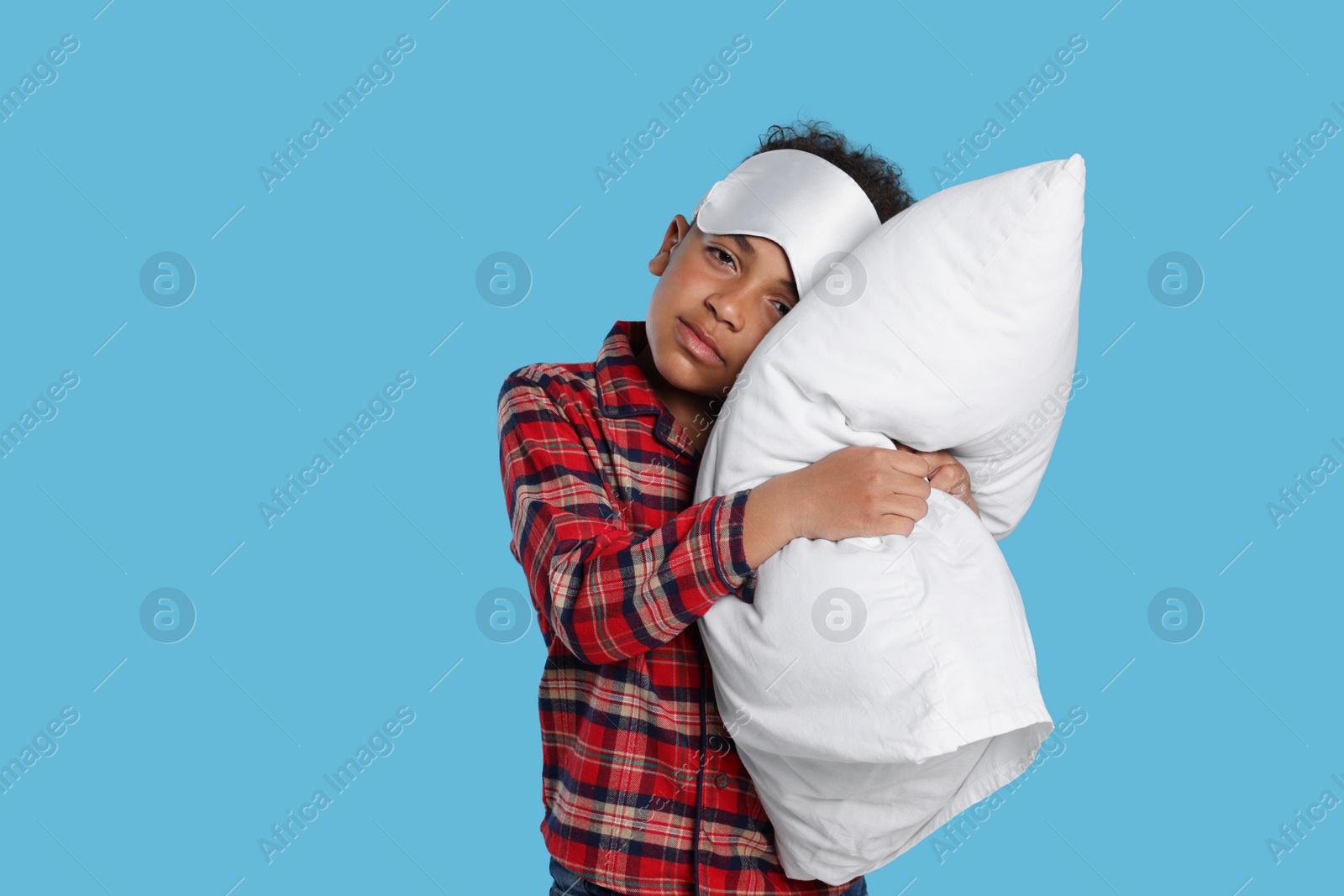 Photo of Boy with pillow and sleep mask on light blue background. Insomnia problem