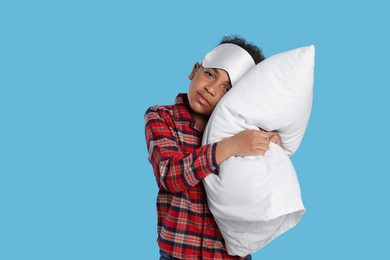 Photo of Boy with pillow and sleep mask on light blue background. Insomnia problem