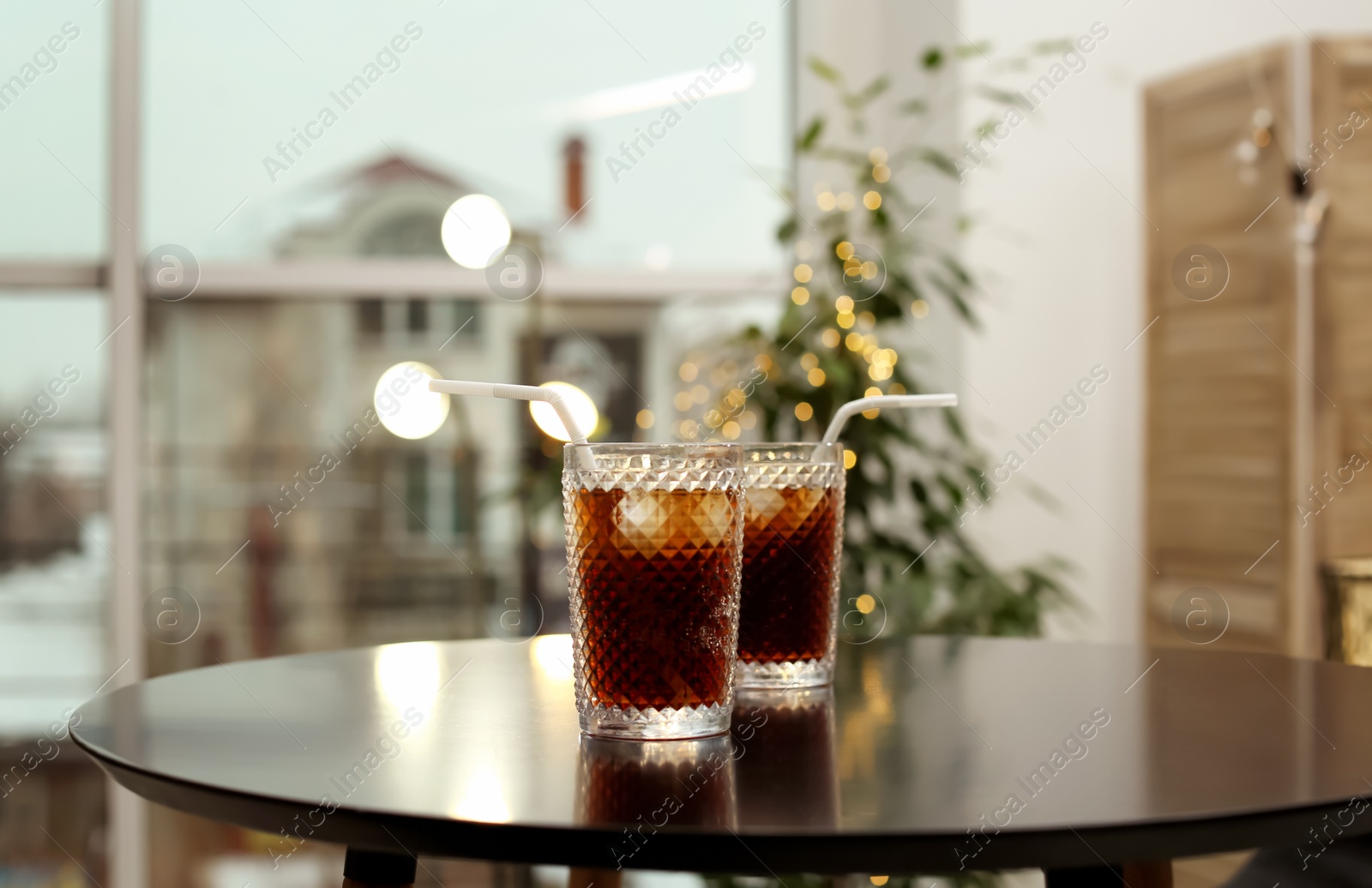 Photo of Glasses of cold cola on table against blurred background