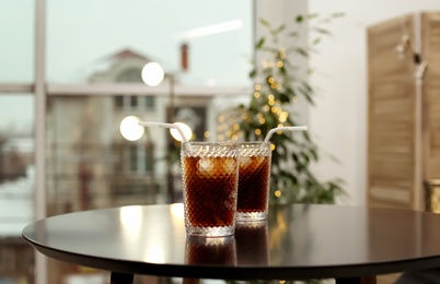 Glasses of cold cola on table against blurred background