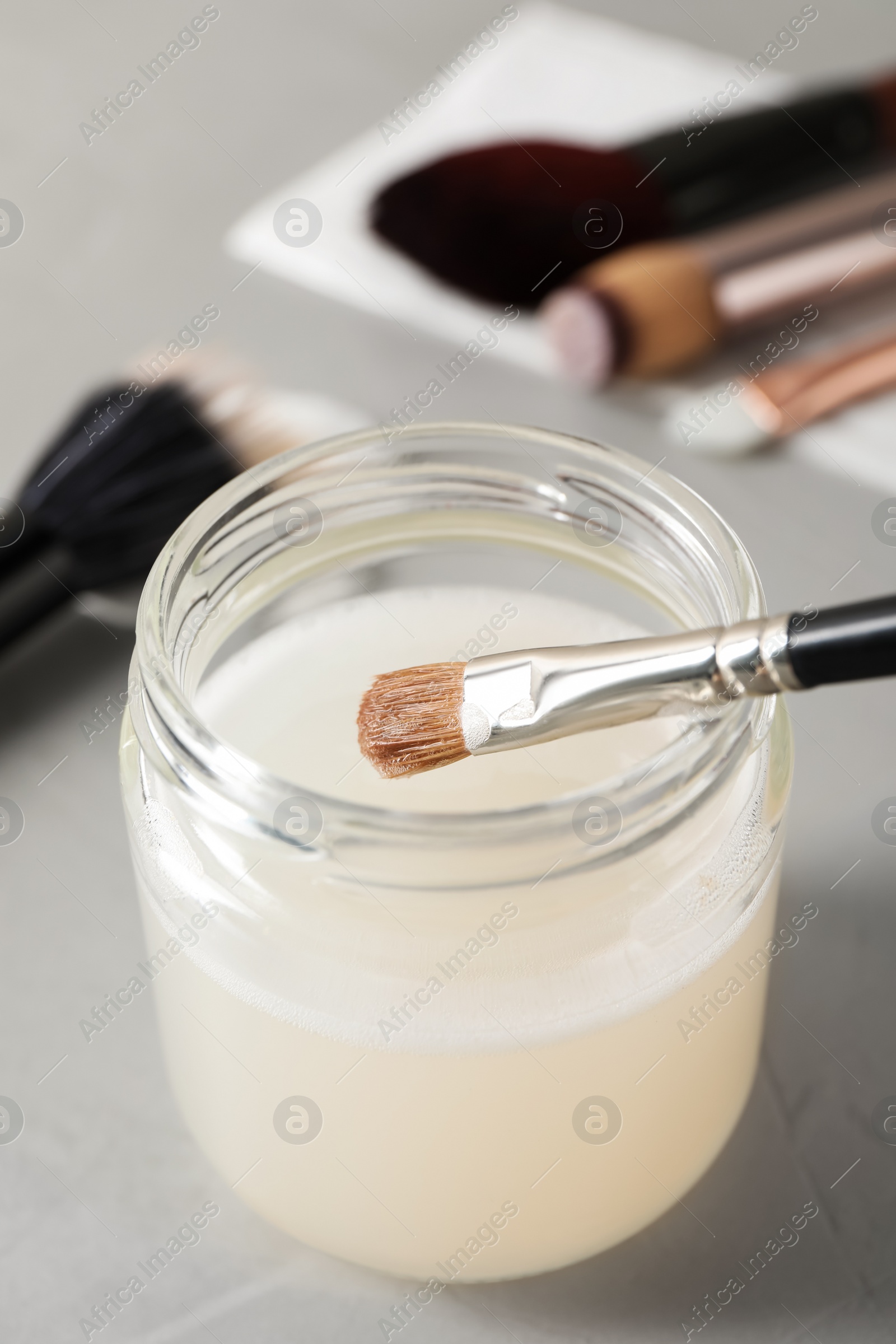 Photo of Cleaning makeup brush in jar with special liquid on grey table, closeup