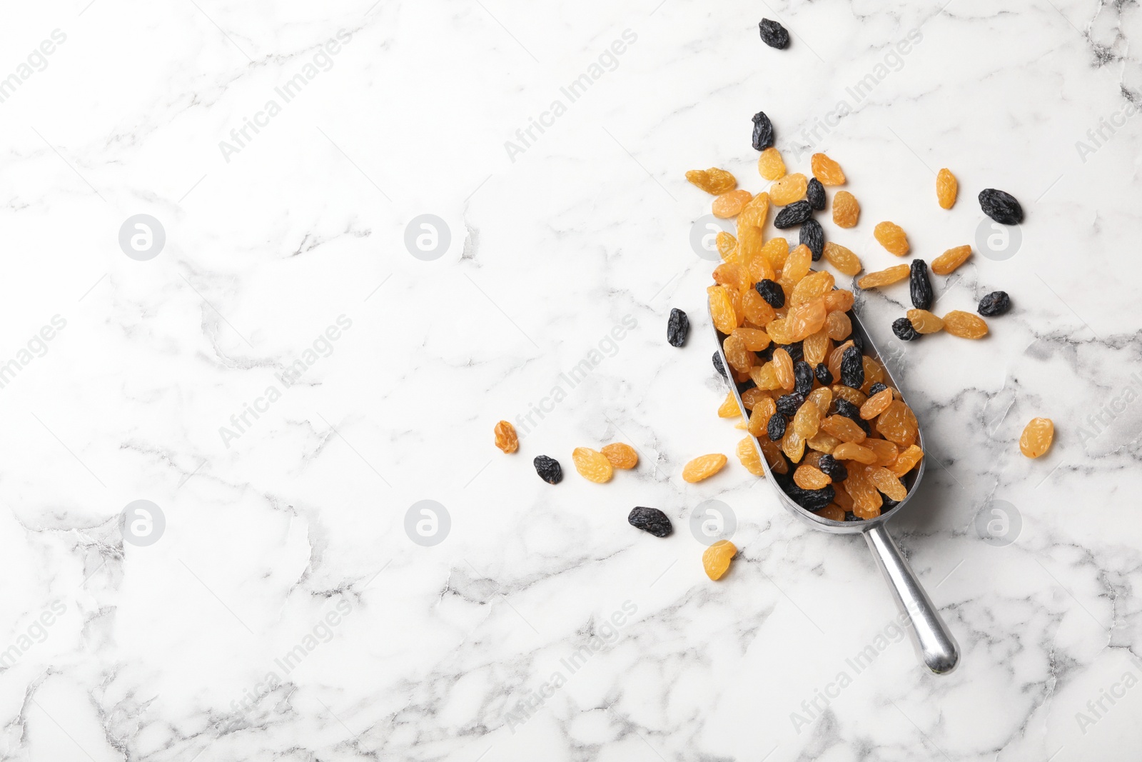 Photo of Scoop with raisins and space for text on marble background, top view. Dried fruit as healthy snack