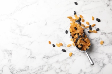 Photo of Scoop with raisins and space for text on marble background, top view. Dried fruit as healthy snack