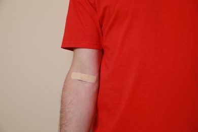 Photo of Blood donation concept. Man with adhesive plaster on arm against beige background, closeup