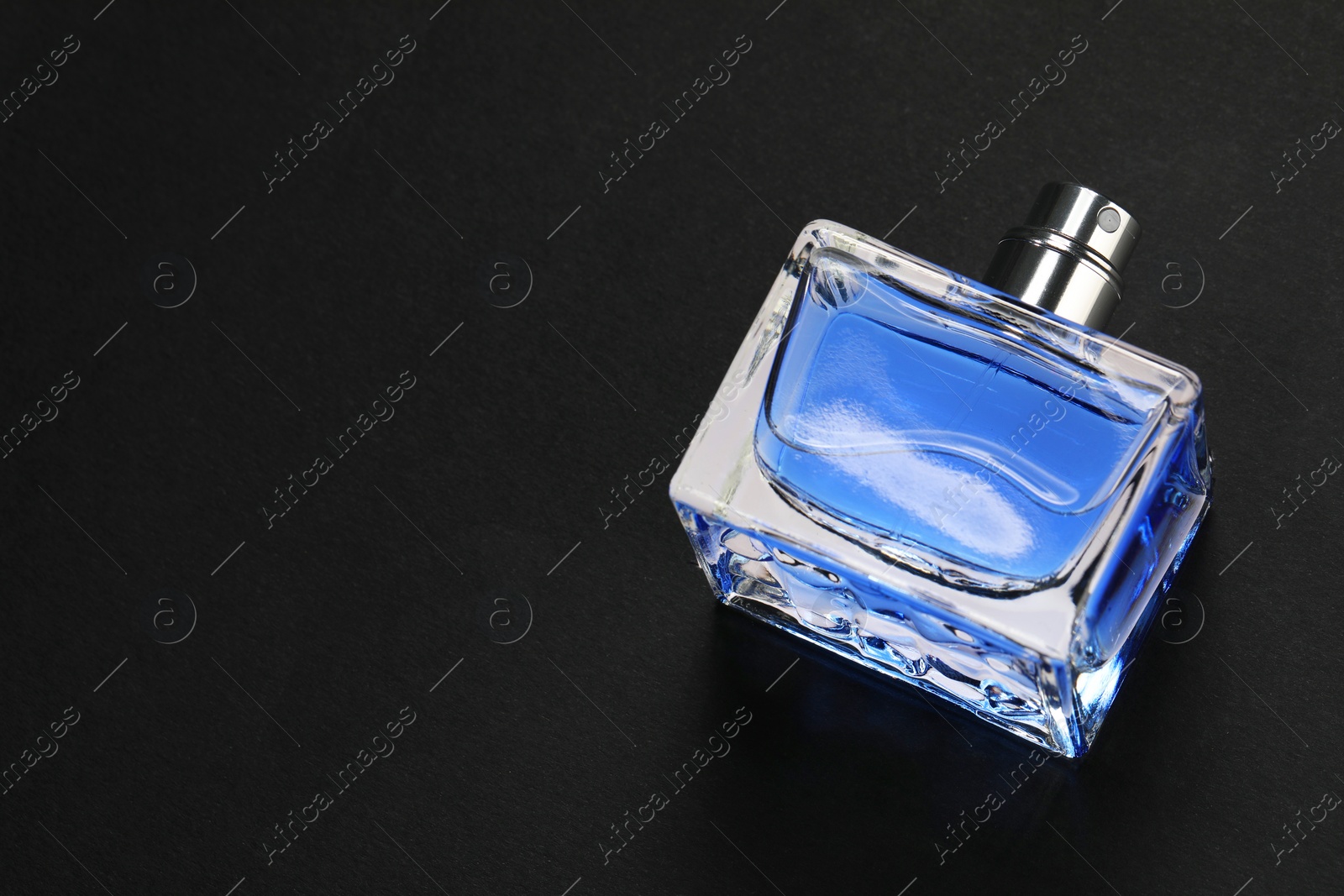 Photo of Blue men's perfume in bottle on black background, above view. Space for text