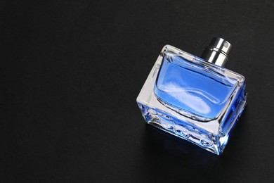 Photo of Blue men's perfume in bottle on black background, above view. Space for text