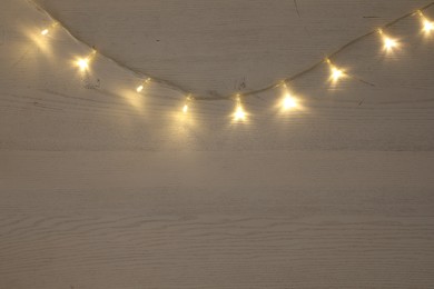 Photo of Beautiful glowing Christmas lights on white wooden table, top view. Space for text