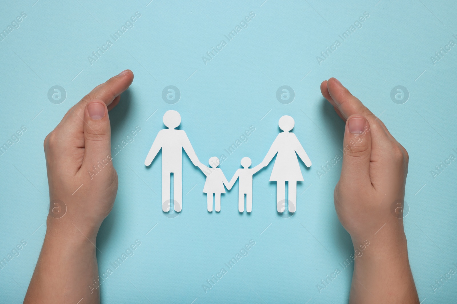 Photo of Man protecting paper family figures on light blue background, top view. Insurance concept