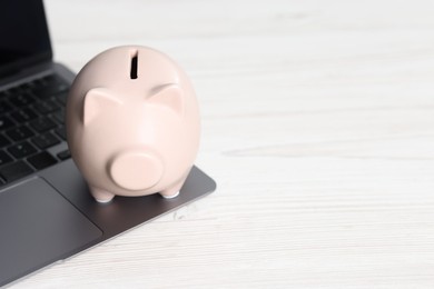 Photo of Piggy bank and laptop on white table. Space for text