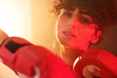 Photo of Beautiful young woman with boxing gloves on color background in neon lights and smoke, closeup