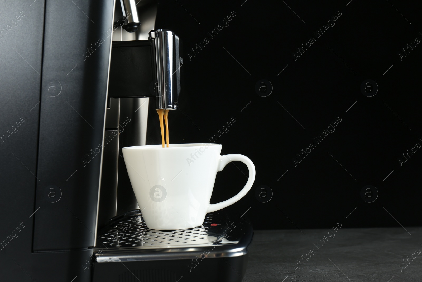 Photo of Modern espresso machine pouring coffee into cup on grey table against black background. Space for text