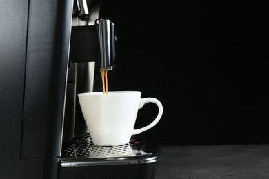 Modern espresso machine pouring coffee into cup on grey table against black background. Space for text