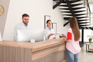 Professional receptionists working with patient at desk in modern clinic