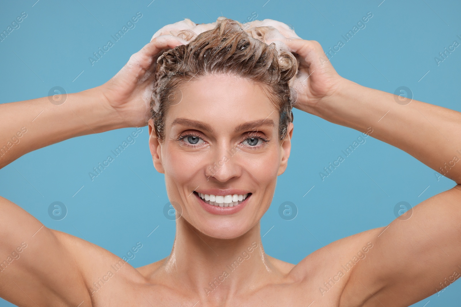 Photo of Portrait of beautiful happy woman washing hair on light blue background