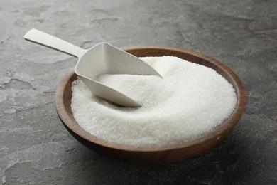 Granulated sugar in bowl and scoop on grey textured table, closeup
