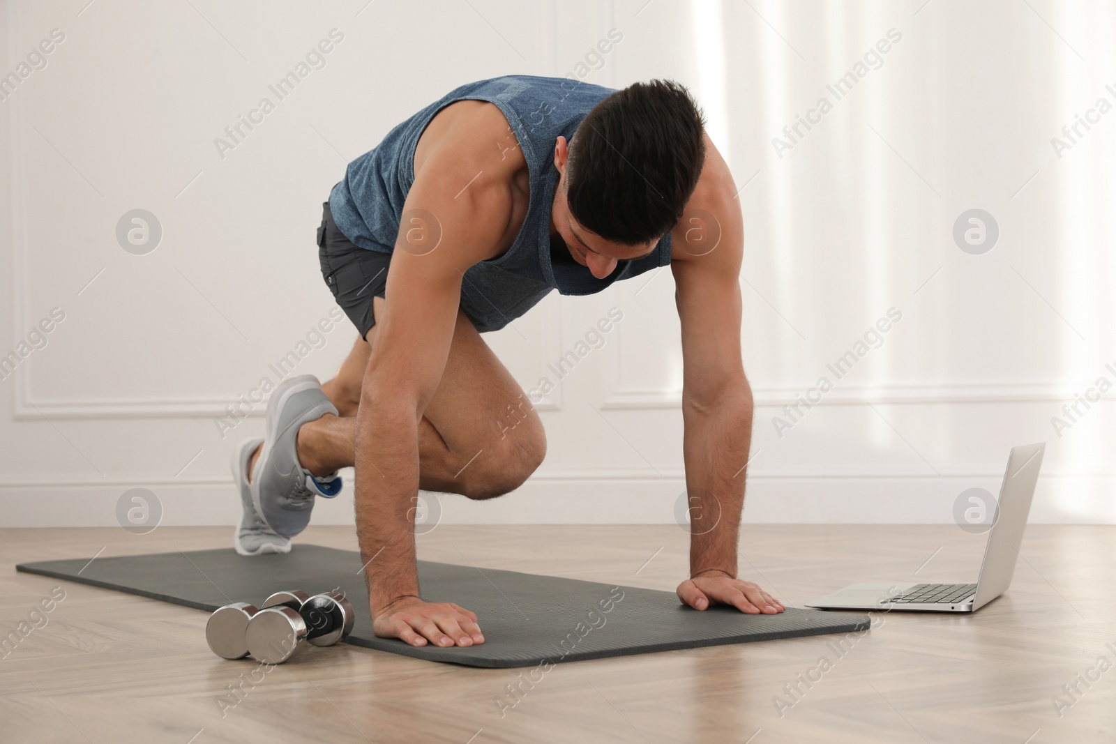 Photo of Handsome man doing abs exercise on yoga mat while watching online class indoors