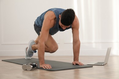 Photo of Handsome man doing abs exercise on yoga mat while watching online class indoors