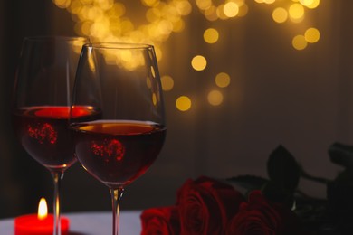 Glasses of red wine, rose flowers and burning candle against blurred lights, space for text. Romantic atmosphere