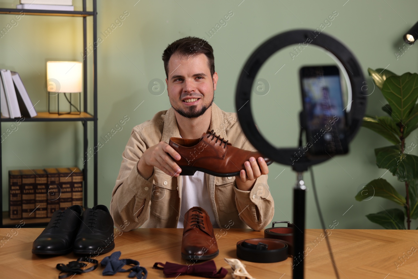 Photo of Smiling fashion blogger showing shoes while recording video at home