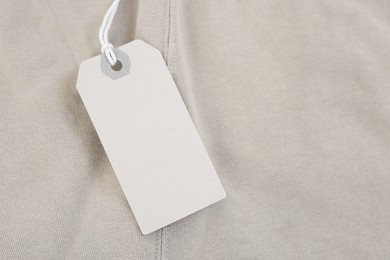 Photo of Cardboard tag on beige garment, top view. Space for text