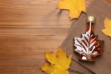 Bottle of tasty maple syrup and dry leaves on wooden table, flat lay. Space for text