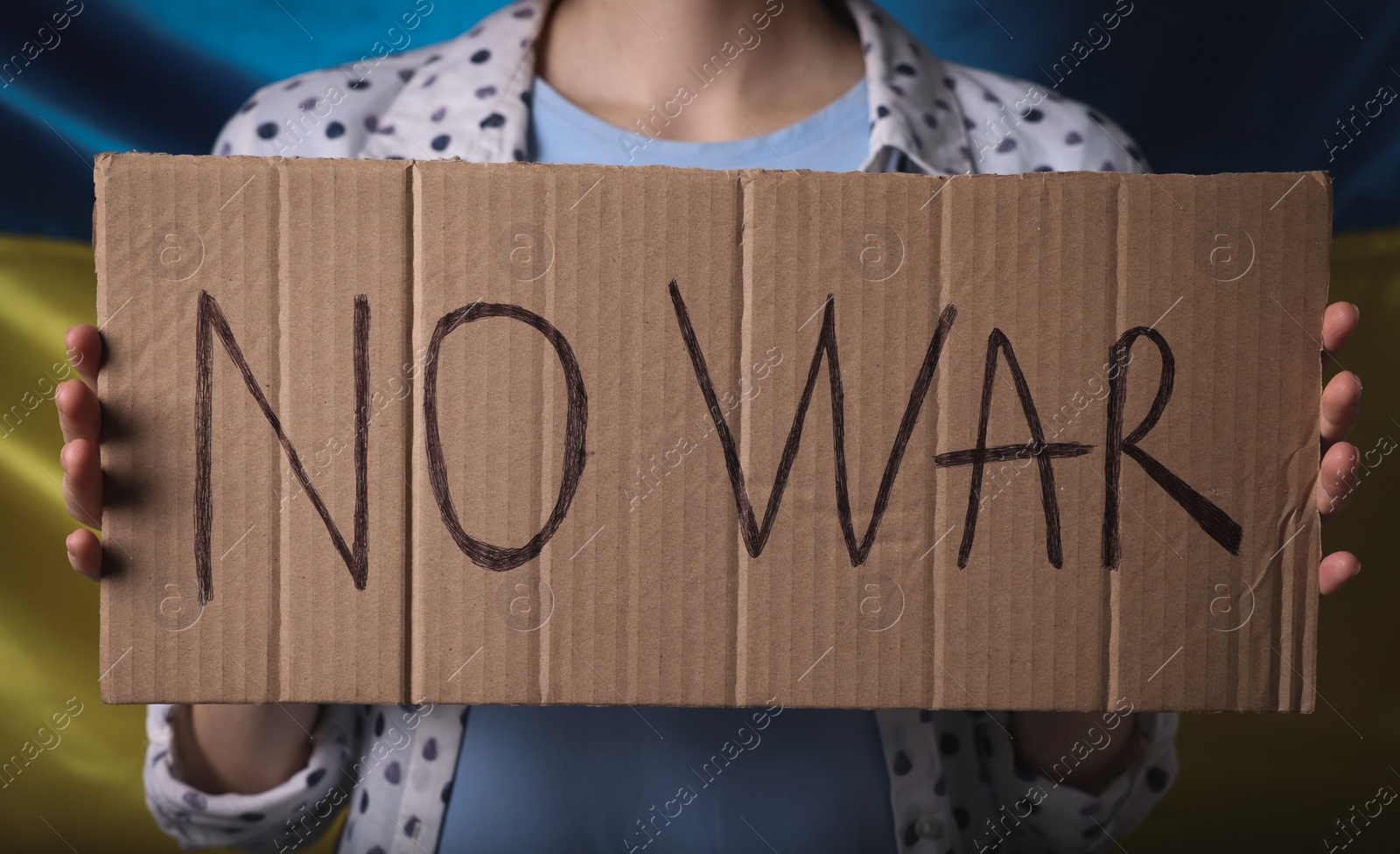 Photo of Woman holding poster with words No War near Ukrainian flag, closeup