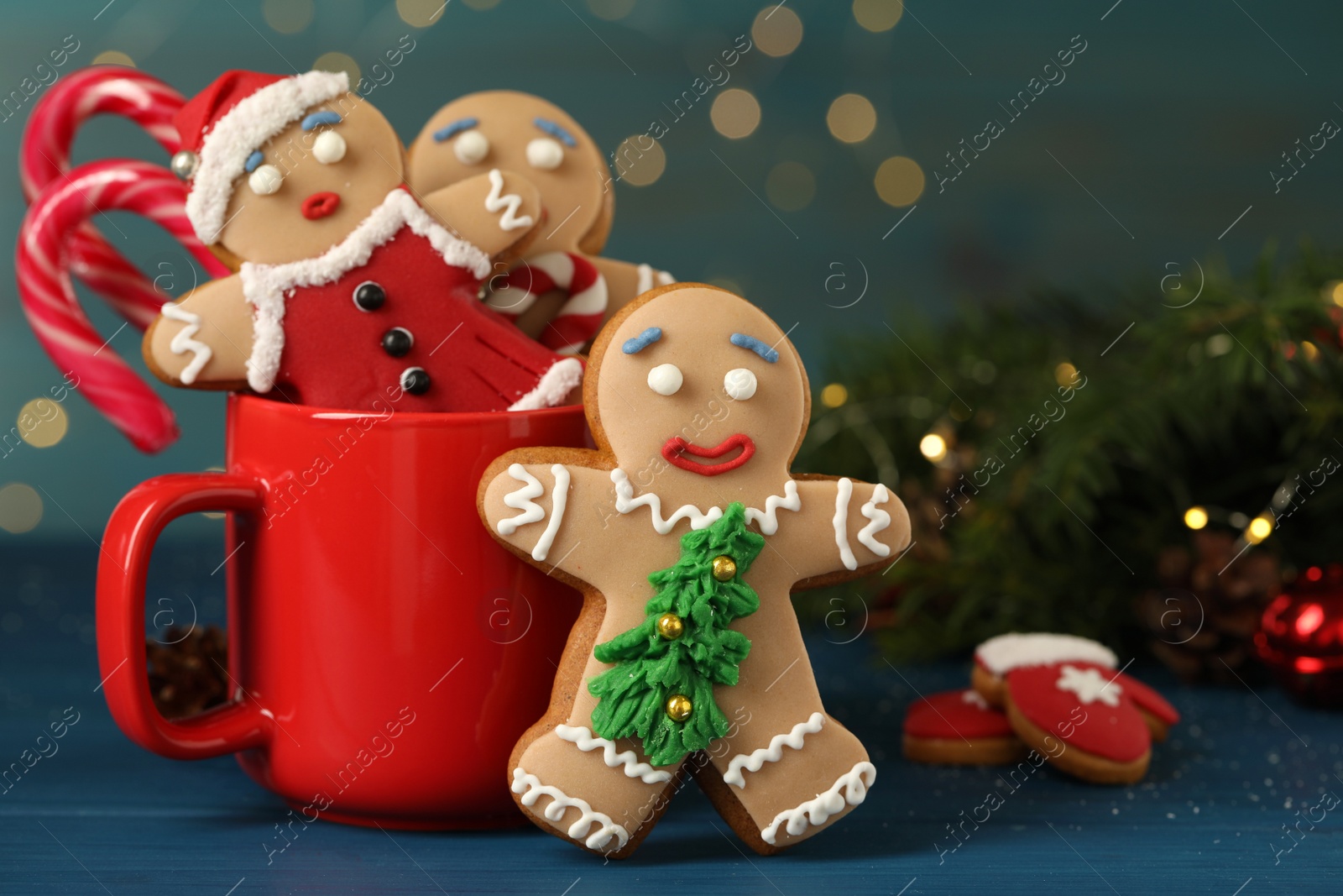 Photo of Delicious homemade Christmas cookies with cup on blue wooden table against blurred festive lights