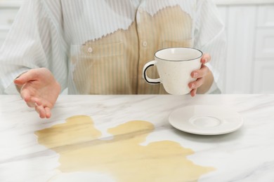 Photo of Woman with spilled coffee over her shirt at marble table indoors, closeup