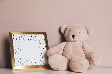Empty photo frame and teddy bear on white table near grey wall. Space for design