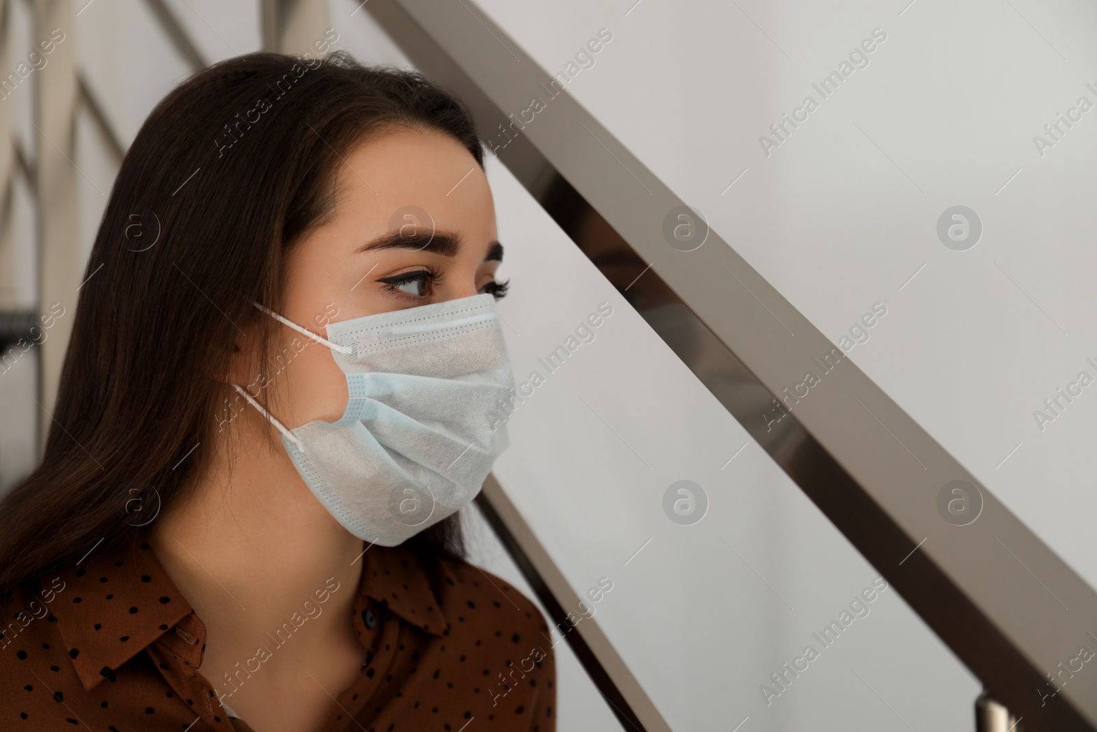 Photo of Sad young woman in protective mask indoors. Self-isolation during coronavirus pandemic