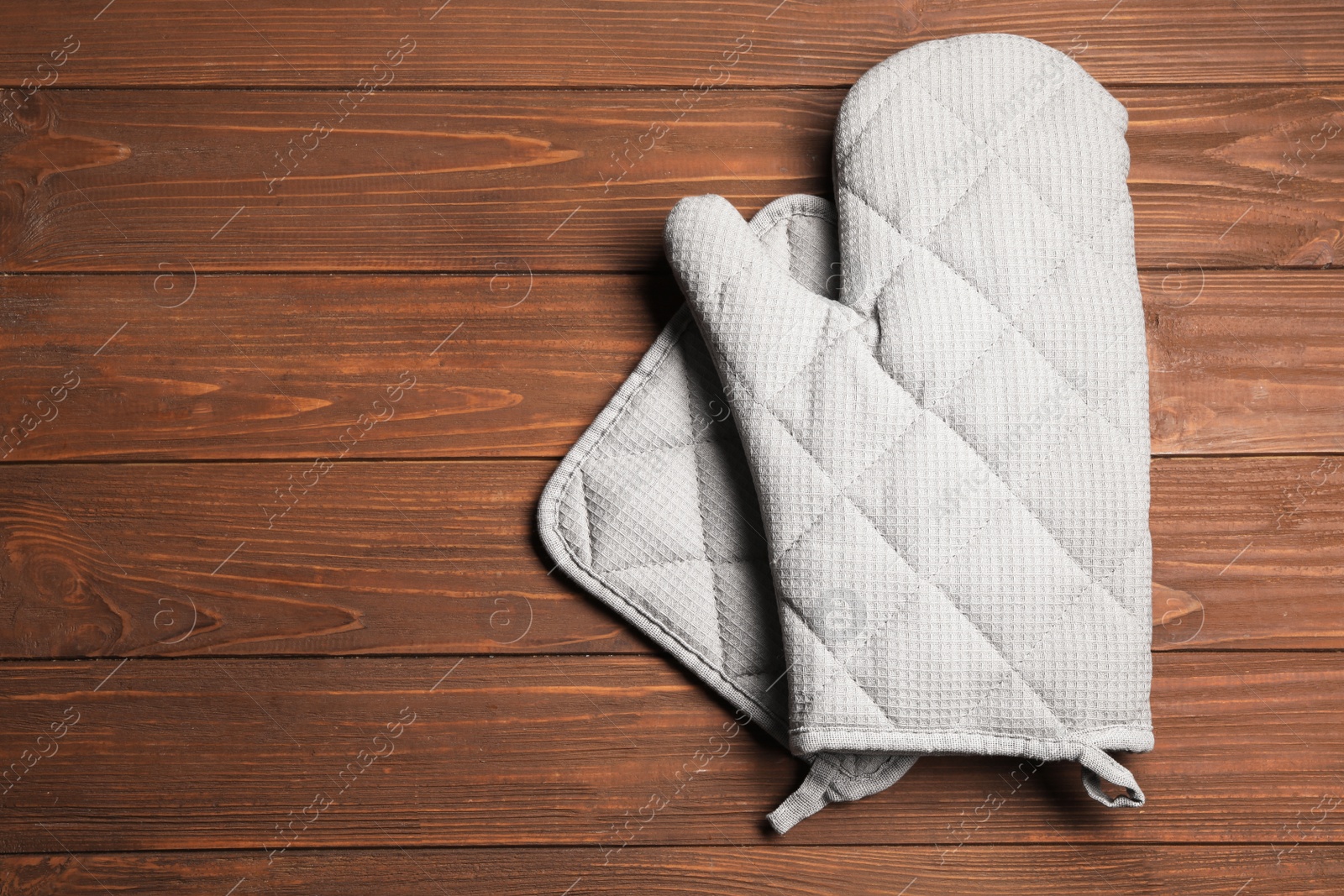 Photo of Oven glove and potholder on wooden background, flat lay. Space for text