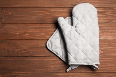 Oven glove and potholder on wooden background, flat lay. Space for text