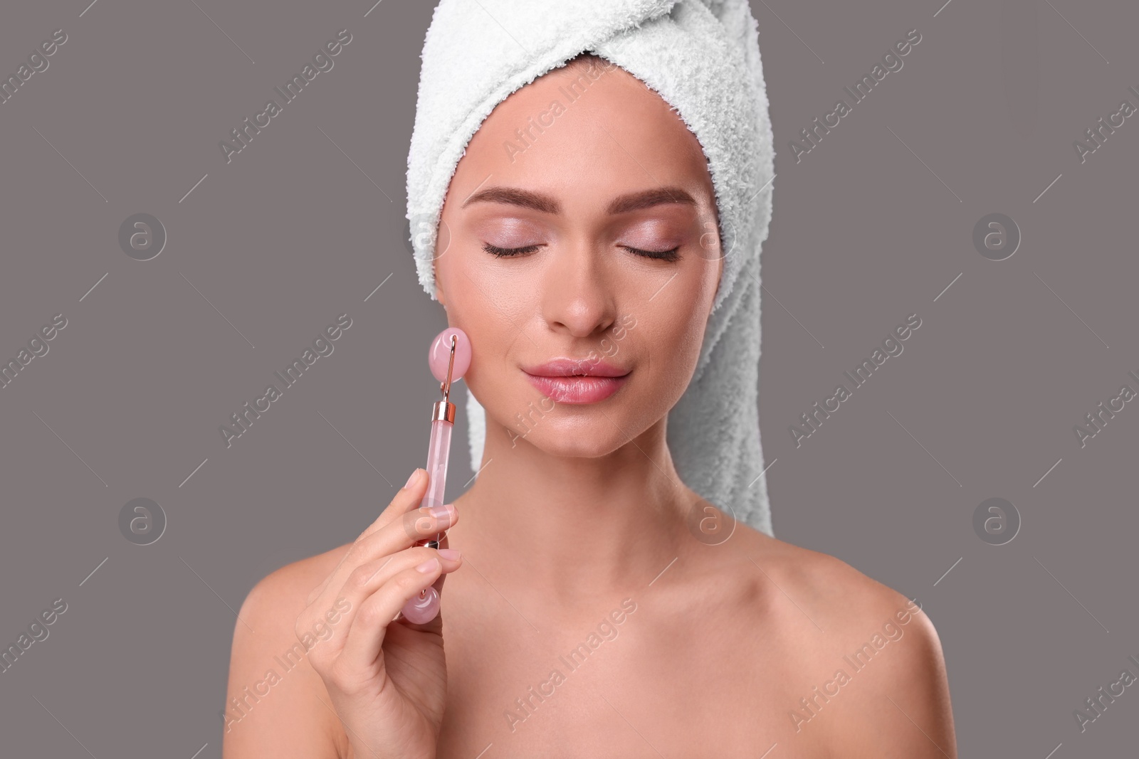 Photo of Young woman massaging her face with rose quartz roller on grey background