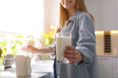 Young woman with gallon bottle of milk and glass at white countertop in kitchen, closeup