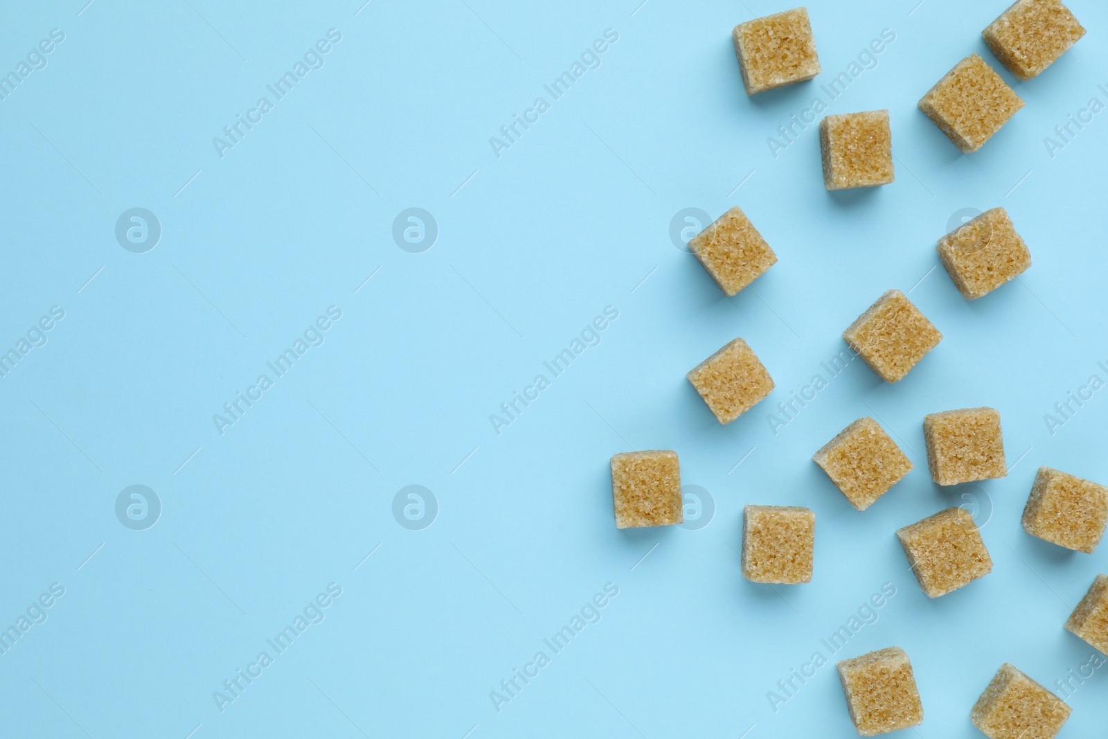 Photo of Brown sugar cubes on light blue background, flat lay. Space for text