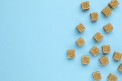 Photo of Brown sugar cubes on light blue background, flat lay. Space for text