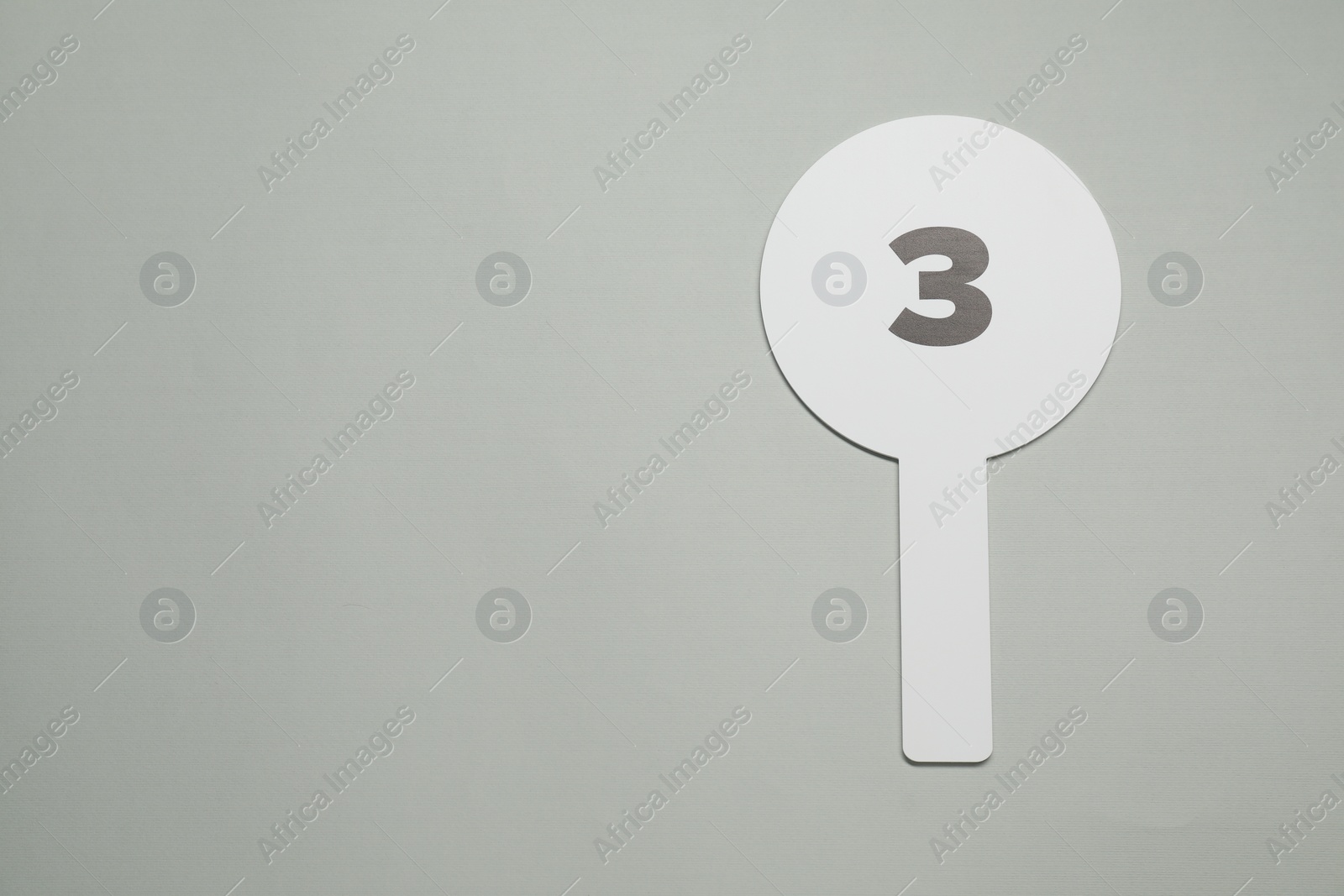 Photo of Auction paddle with number 3 on light grey background, top view. Space for text