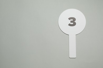 Photo of Auction paddle with number 3 on light grey background, top view. Space for text