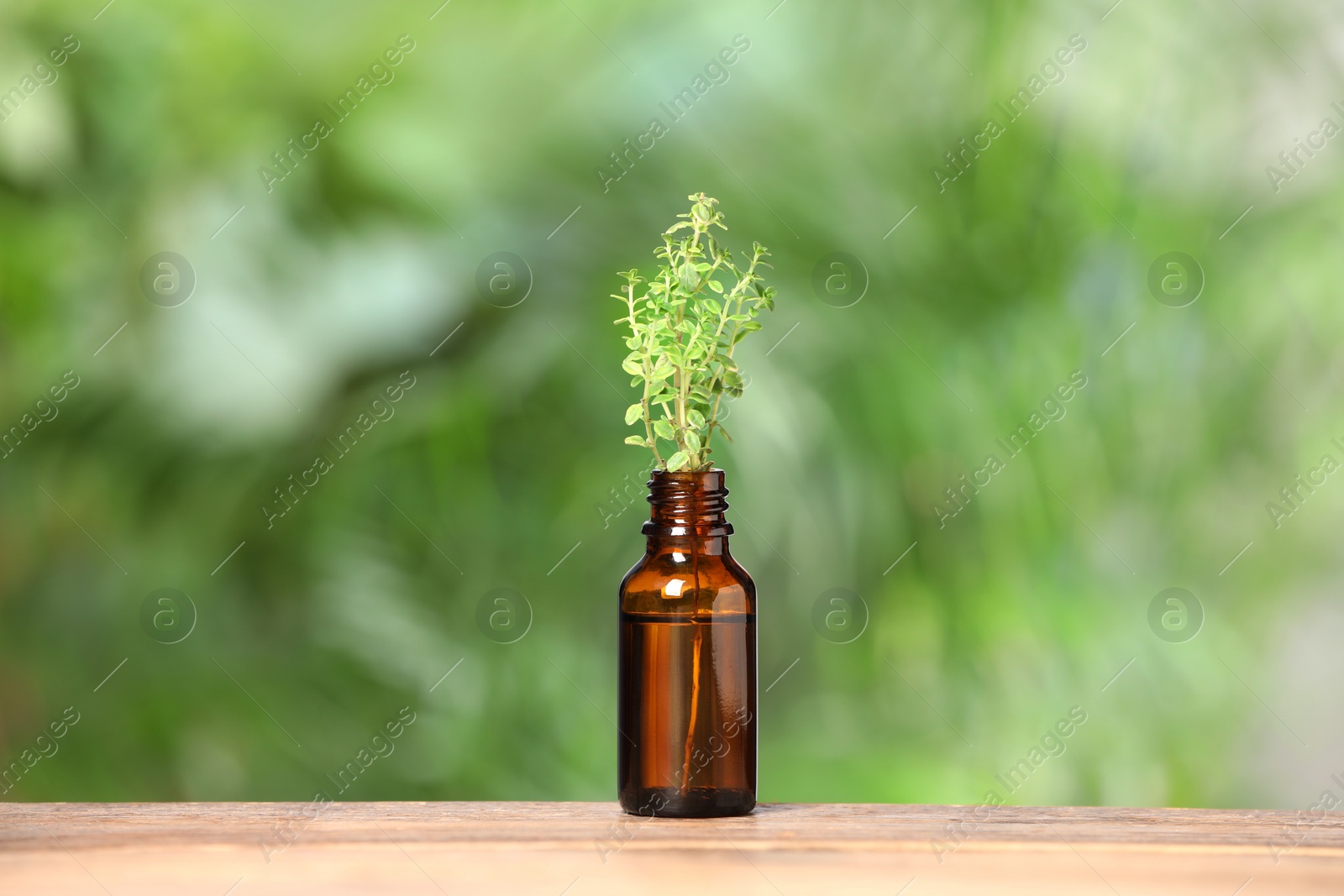 Photo of Bottle with essential oil and thyme on wooden table against blurred green background