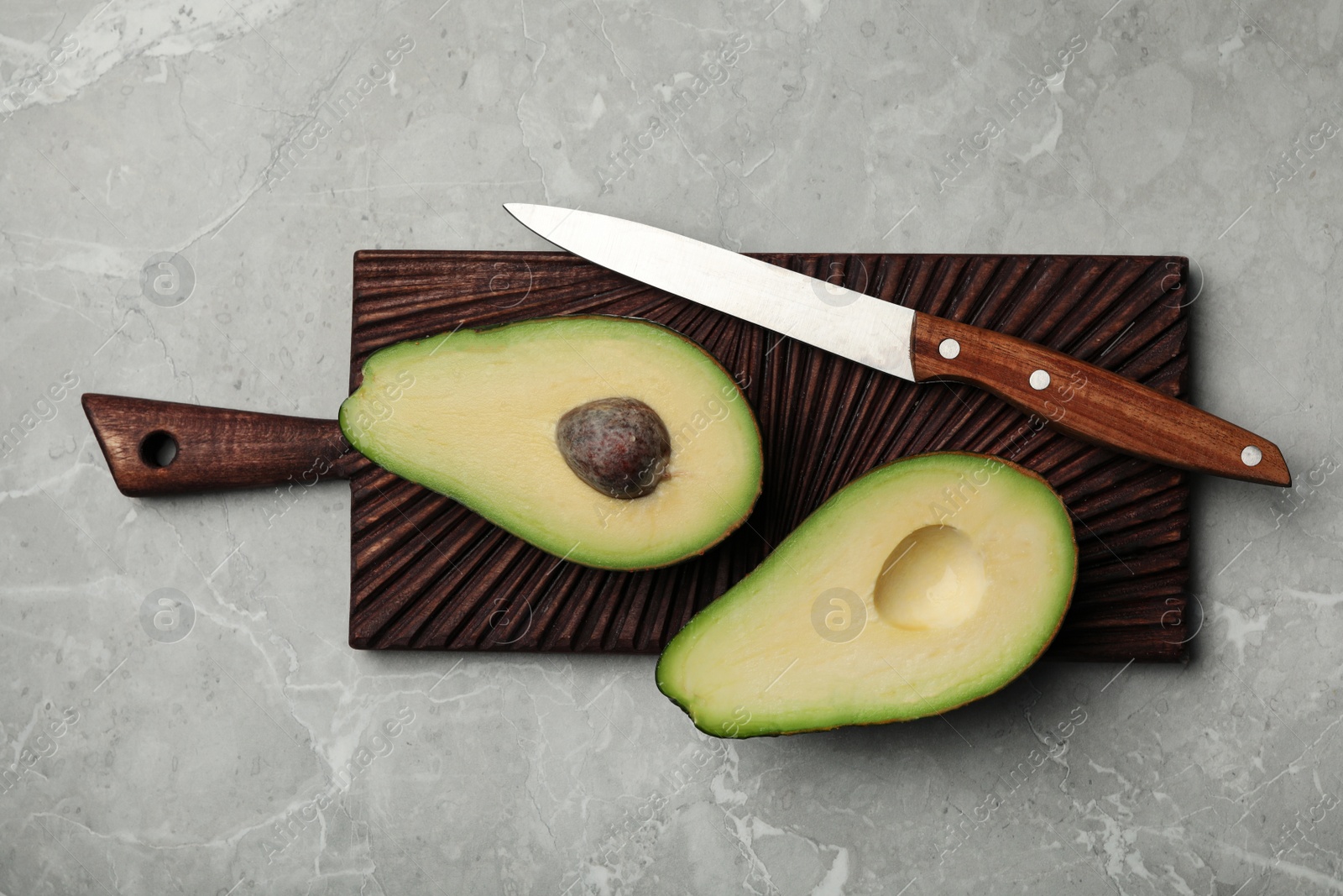 Photo of Halves of delicious ripe avocado on grey marble table, top view