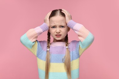 Photo of Little girl suffering from headache on pink background