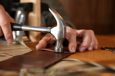 Photo of Man working with piece of leather at table, closeup