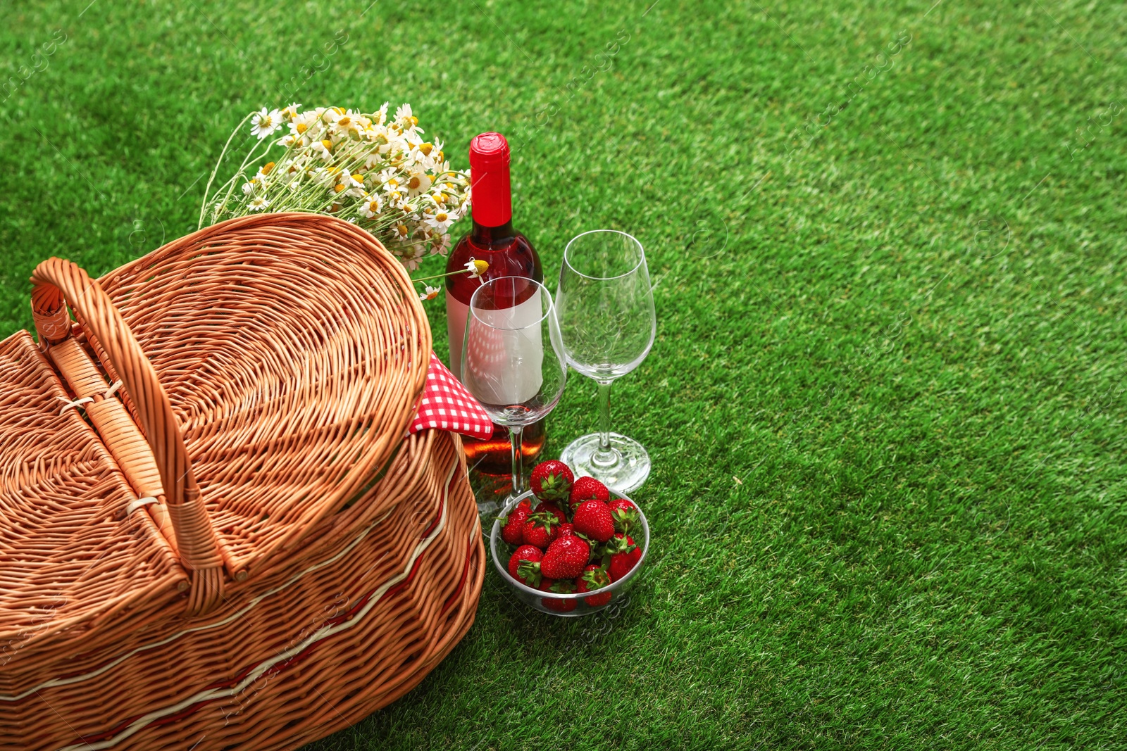 Photo of Picnic basket with wine and bowl of strawberries on grass. Space for text