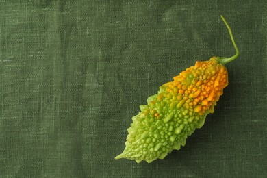Photo of Fresh bitter melon on dark green cloth, top view. Space for text